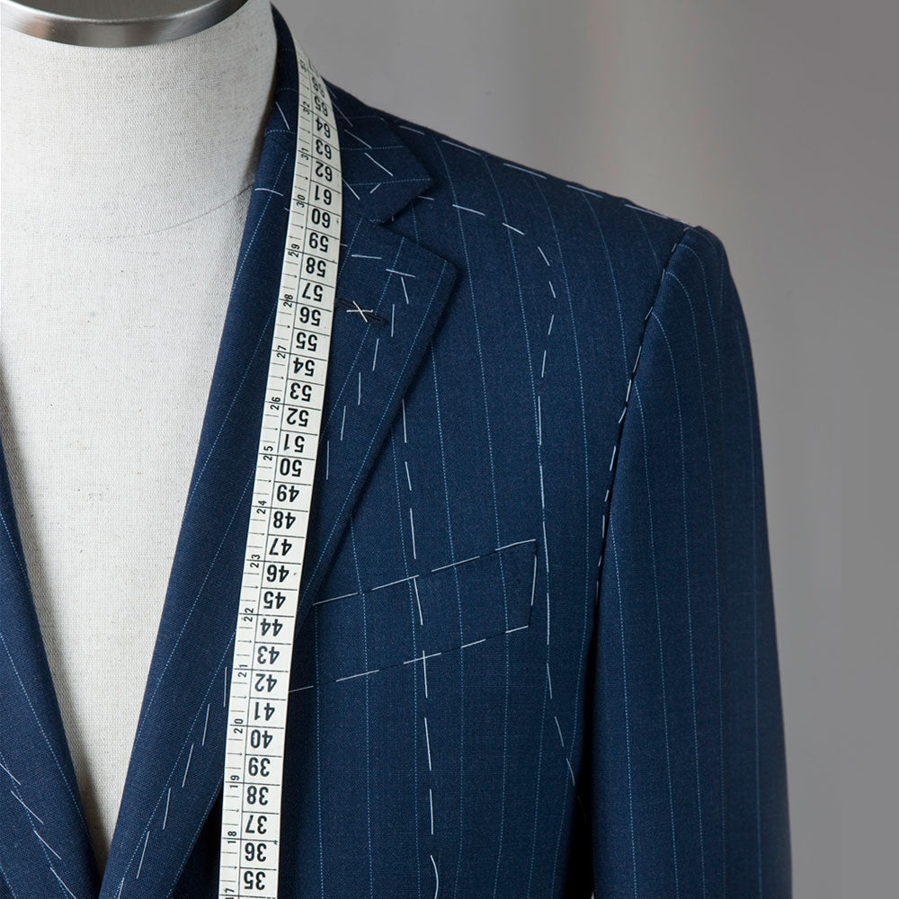 A men's suit on a modelling dummy with a tape measure draped around the neck. The suit is marked up for alteration by a taylor.