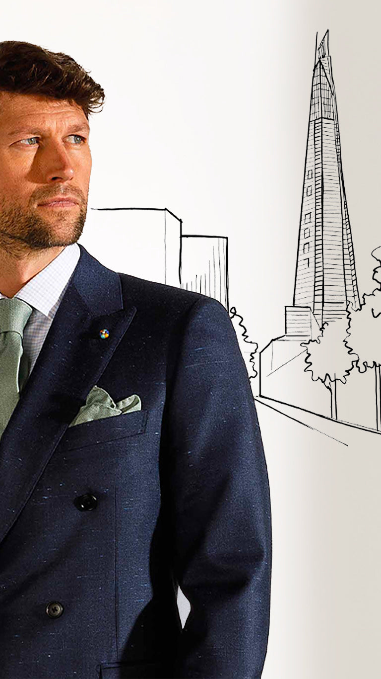 Man in a suit standing in front of a white wall with a drawing of a skyscraper.